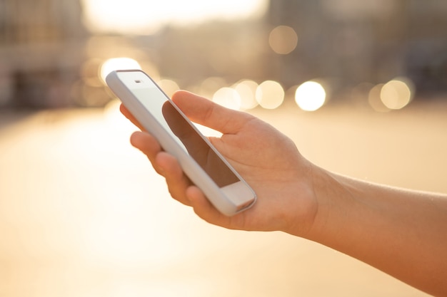 Mano femenina que sostiene el teléfono celular en el desenfoque de fondo claro. Espacio para texto