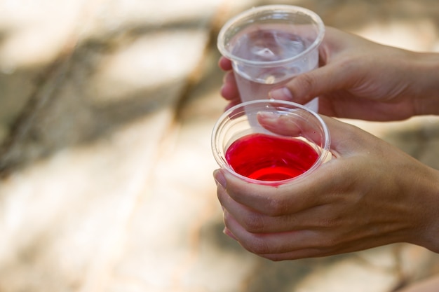 Mano femenina que sostiene el vaso de agua con líquido rojo bebida y fondo de agua