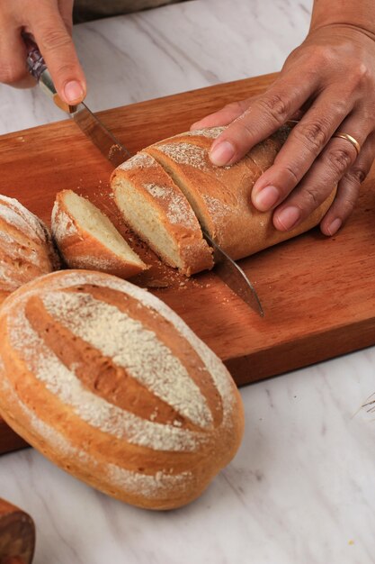 Mano femenina rebanar pan de hogar de leche japonés con un cuchillo de pan para el desayuno. Milk Hearth Bread es un pan japonés con leche o crema batida, suave y esponjoso. Enfoque seleccionado