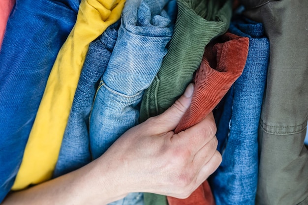 Mano femenina recoge pantalones de terciopelo rojo de un montón de jeans cuidadosamente doblados en colores brillantes