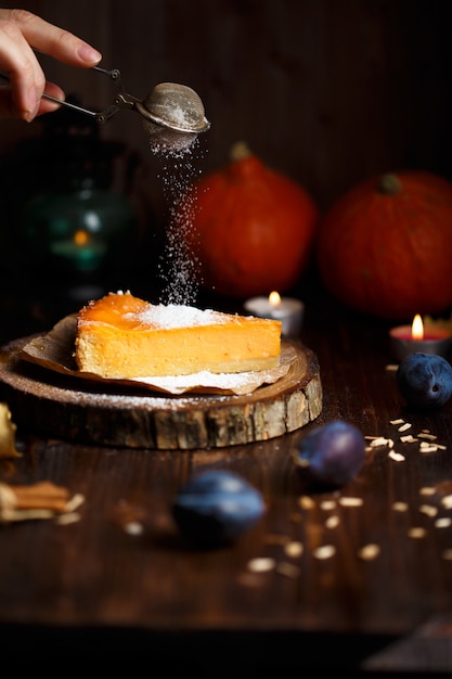 La mano femenina rocía azúcar en polvo sobre el pastel de queso de calabaza.