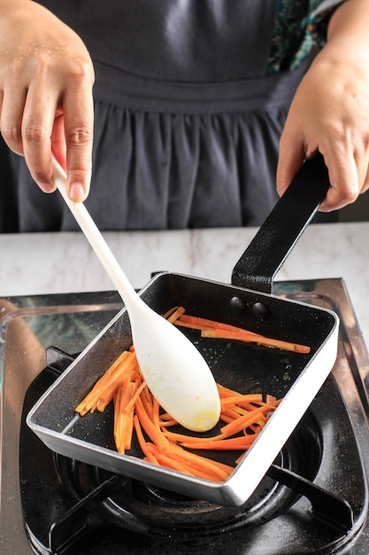 Foto mano femenina saltear zanahorias en una sartén, proceso de cocción casera en la cocina para hacer kimbap / gimbap coreanos