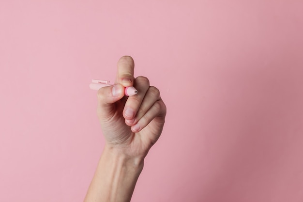 Mano femenina sostenga la pluma y escriba sobre fondo rosa