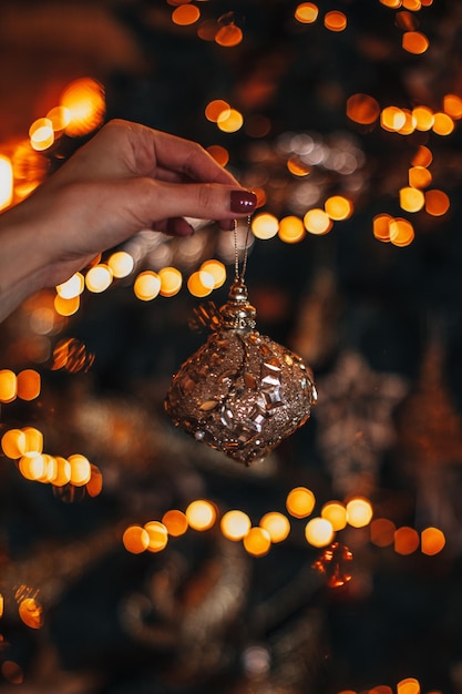 Mano femenina sosteniendo una bola de Navidad dorada contra un fondo de luces bokeh doradas festivas