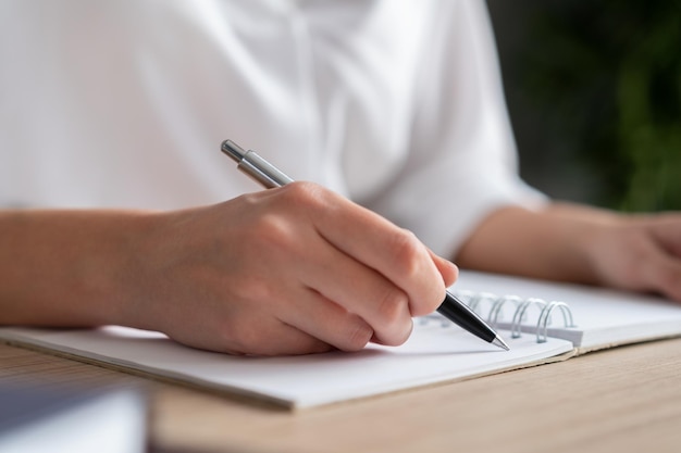 Mano femenina sosteniendo un bolígrafo haciendo notas en el cuaderno primer plano de la lista de papel en blanco mujer gerente de oficina escribiendo Mujer escribiendo en el cuaderno de oficina sin rostro Concepto de escritura