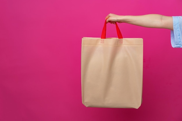 Mano femenina sosteniendo una bolsa de compras ecológica o reutilizable contra un fondo rosa