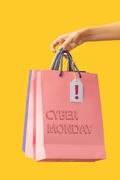 Mano femenina sosteniendo bolsas de compras brillantes en amarillo. Cyber monday y concepto de venta.