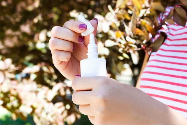 Mano femenina sosteniendo una botella de aerosol nasal en el parque