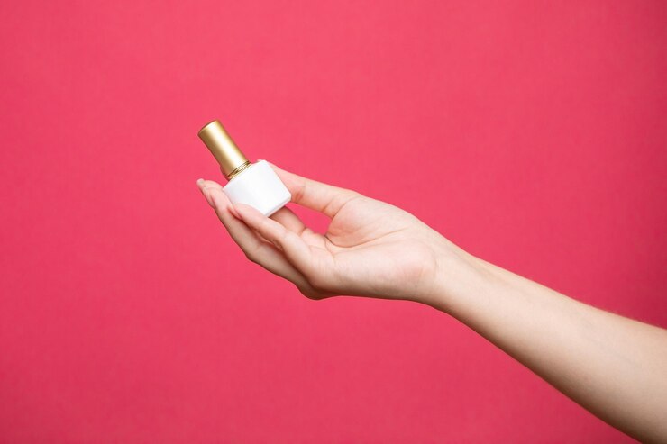 Mano femenina sosteniendo una botella de esmalte de uñas sobre fondo rosa.