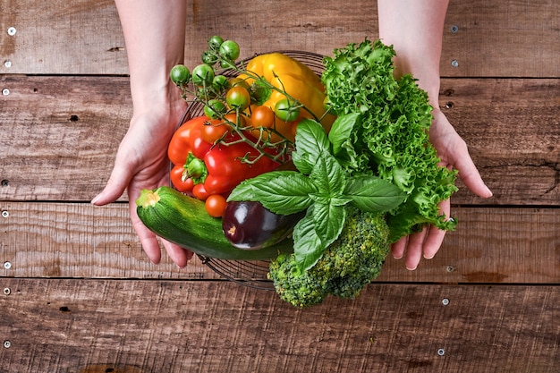 Mano femenina sosteniendo una canasta con verduras y frutas frescas sobre fondo rústico de madera vieja, vista superior. Espacio para texto. Fondo de cocción de alimentos y maquetas.