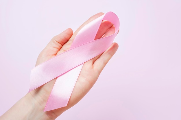 Foto mano femenina sosteniendo una cinta sobre un fondo rosa de cerca