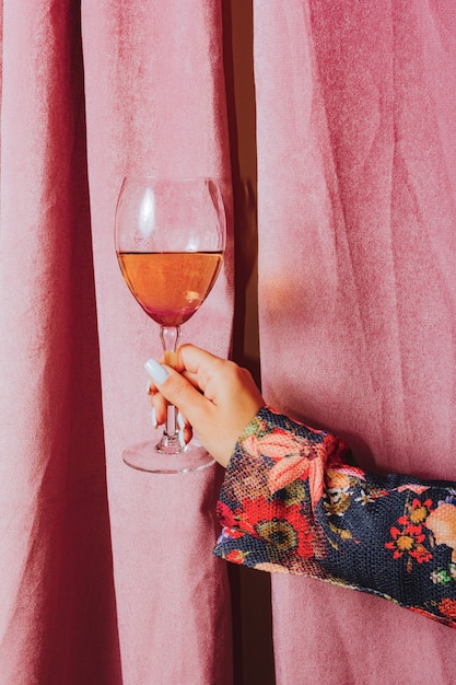 Foto mano femenina sosteniendo una copa de vino. cortina rosa de fondo.