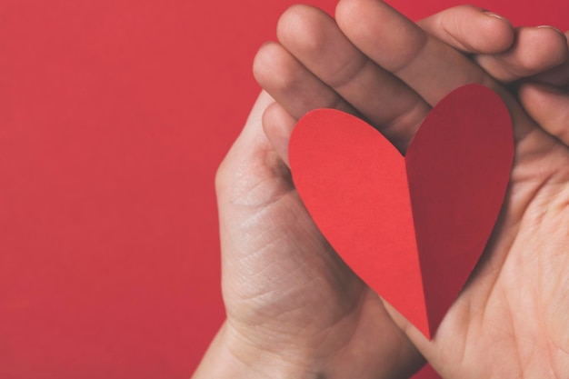 Mano femenina sosteniendo un corazón cortado de papel rojo sobre un fondo rojo liso