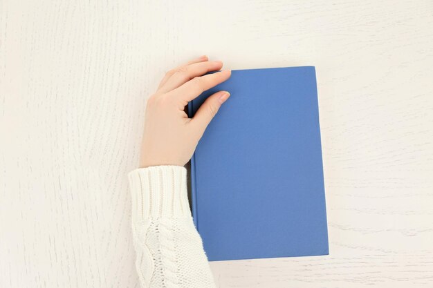 Mano femenina sosteniendo una cubierta de libro azul claro aislada en la vista superior del escritorio blanco