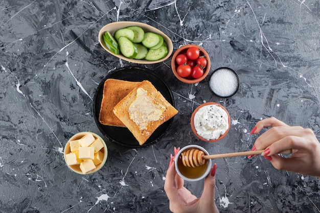 Mano femenina sosteniendo una cuchara de miel en la mesa del desayuno.