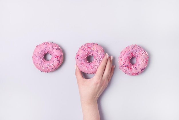 Mano femenina sosteniendo donas rosadas con glaseado sobre fondo azul rosa pastel Donas dulces y sabrosas