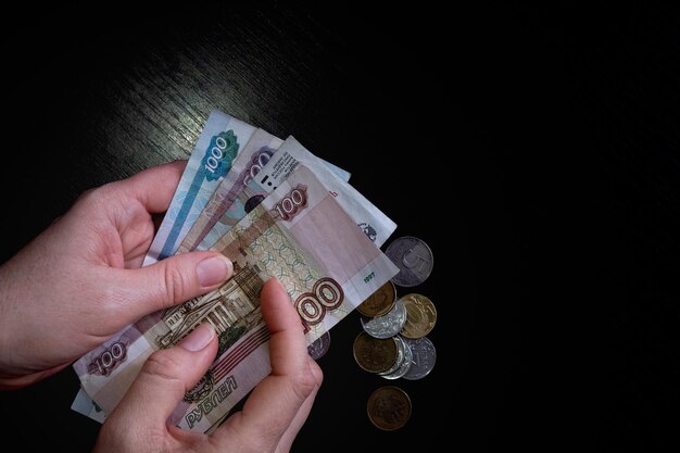 Mano femenina sosteniendo un fajo de billetes rublos rusos primer plano sobre fondo negro pobreza