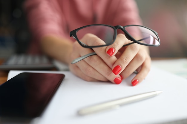 Mano femenina sosteniendo gafas junto al teléfono inteligente y lápiz