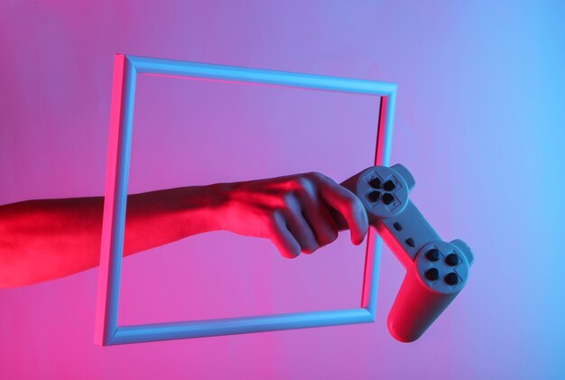 Mano femenina sosteniendo un gamepad retro a través de un marco altísimo con luz holográfica de neón