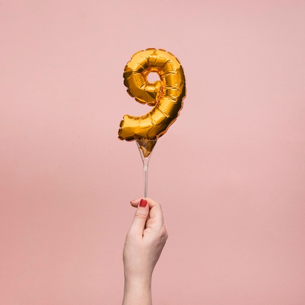 Mano femenina sosteniendo un globo de oro de celebración de aniversario de cumpleaños número 9