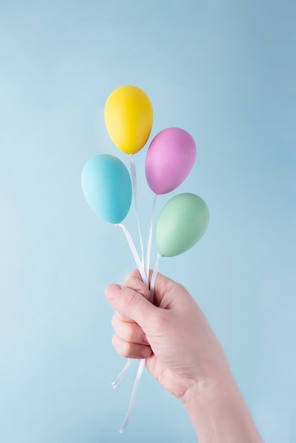 Una mano femenina sosteniendo huevos coloridos que parecen globos.