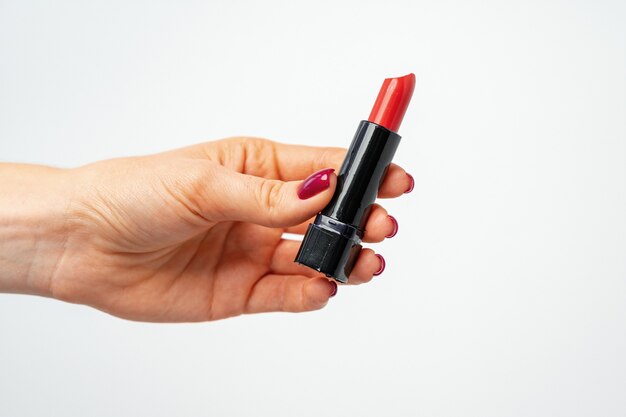 Mano femenina sosteniendo el lápiz labial rojo sobre fondo gris cerrar