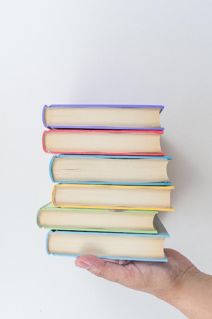 Mano femenina sosteniendo libros apilados sobre un fondo blanco Libros de texto de estudio