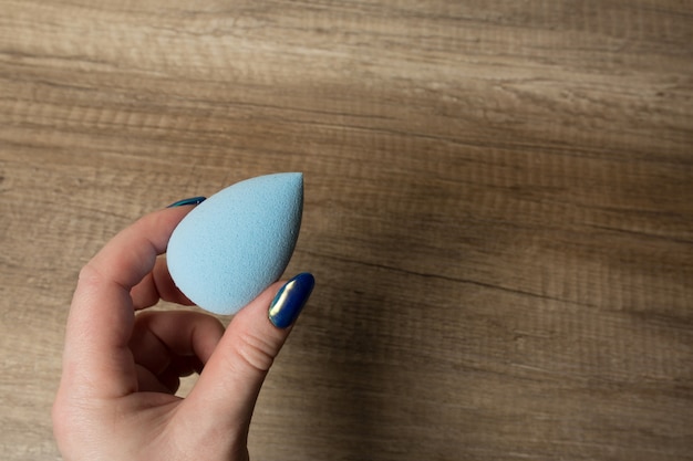 Mano femenina sosteniendo la licuadora de belleza azul sobre un fondo de madera