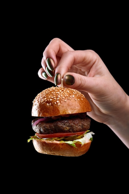 Mano femenina sosteniendo mini hamburguesa como un juguete de árbol de Navidad en superficie negra