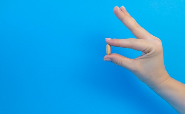 Mano femenina sosteniendo una pastilla blanca sobre un fondo azul con espacio de copia El concepto de atención médica de farmacia de tratamiento