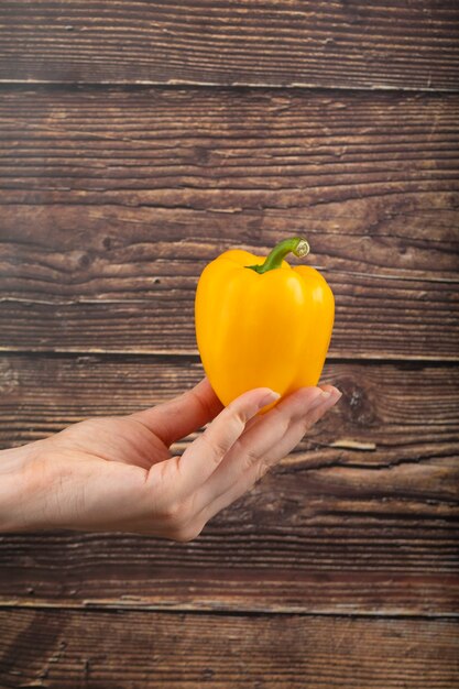 Mano femenina sosteniendo pimiento amarillo sobre superficie de madera