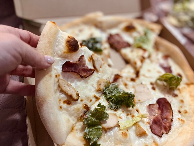 Mano femenina sosteniendo pizza con lechuga de pollo con tocino y mozzarella