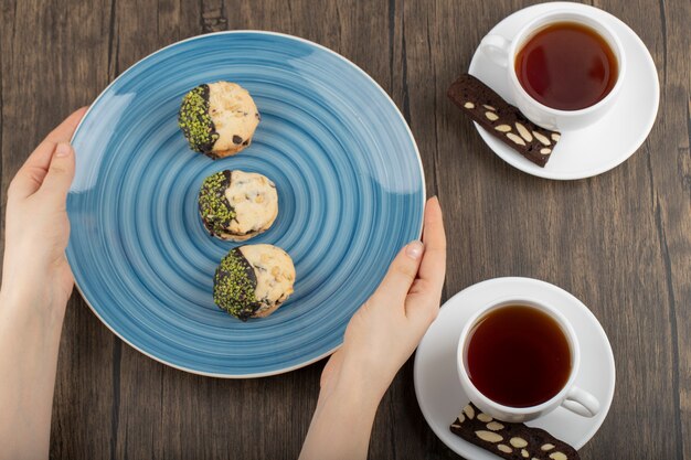 Mano femenina sosteniendo un plato con galletas y tazas de té.