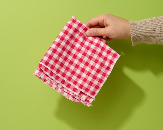 Mano femenina sosteniendo una servilleta textil rojo-blanco sobre un fondo verde