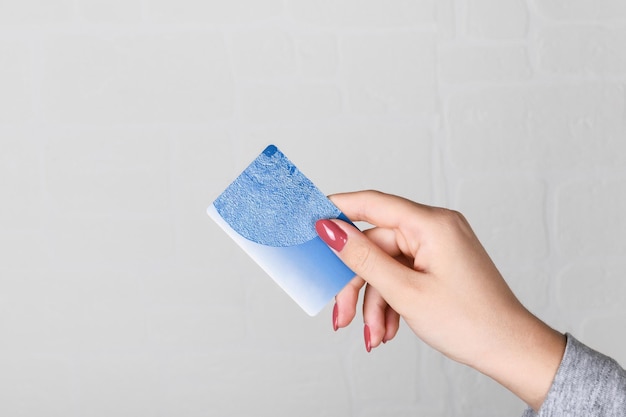 Mano femenina sosteniendo una tarjeta de crédito azul sobre un fondo de pared