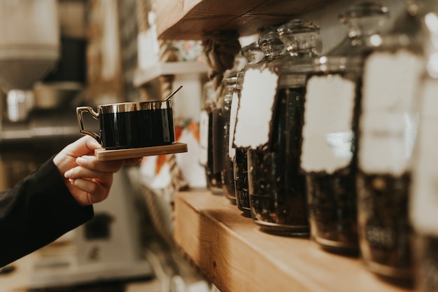 Mano femenina sosteniendo la taza de café en la cafetería frente a los estantes