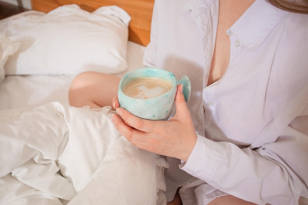 Mano femenina sosteniendo una taza de café mientras está sentado en la cama