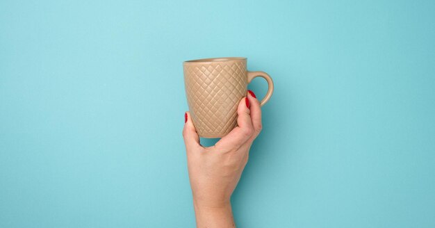 Foto mano femenina sosteniendo una taza de cerámica marrón en un fondo azul tiempo de descanso y beber café