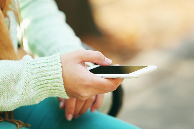 Una mano femenina sosteniendo un teléfono móvil al aire libre en un fondo borroso