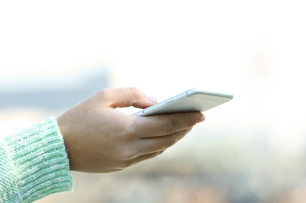 Una mano femenina sosteniendo un teléfono móvil al aire libre en un fondo borroso