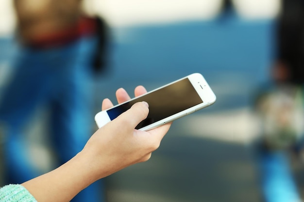 Una mano femenina sosteniendo un teléfono móvil al aire libre en un fondo borroso