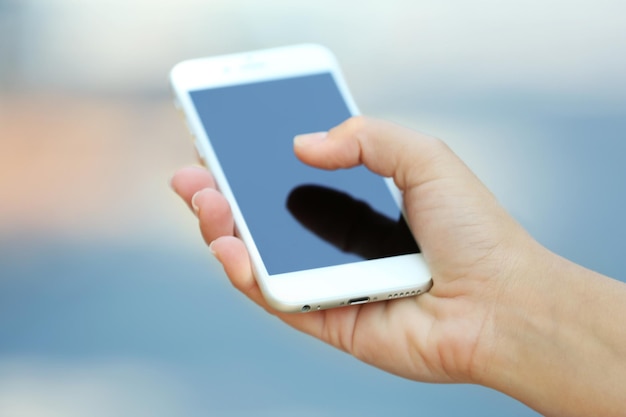 Una mano femenina sosteniendo un teléfono móvil al aire libre en un fondo borroso