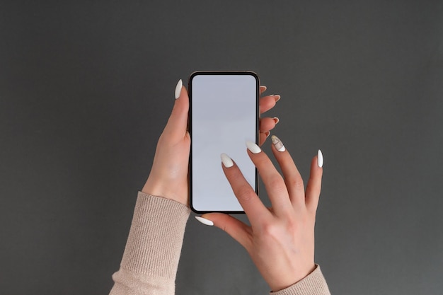 Mano femenina sosteniendo y tocando en el teléfono inteligente móvil con pantalla blanca Aislado en gris Plantilla de foto para cualquier imagen en la pantalla del teléfono móvil Diseño con fondo de monitor de teléfono fácilmente extraíble