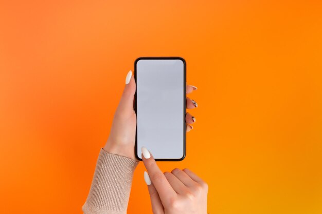 Mano femenina sosteniendo y tocando en el teléfono inteligente móvil con pantalla blanca Aislado en la plantilla de Orange Photo para cualquier imagen en la pantalla del teléfono móvil Diseño con fondo de monitor de teléfono fácilmente extraíble