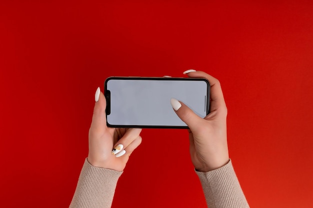 Mano femenina sosteniendo y tocando en el teléfono inteligente móvil con pantalla blanca Aislado en rojo Plantilla de foto para cualquier imagen en la pantalla del teléfono móvil Diseño con fondo de monitor de teléfono fácilmente extraíble