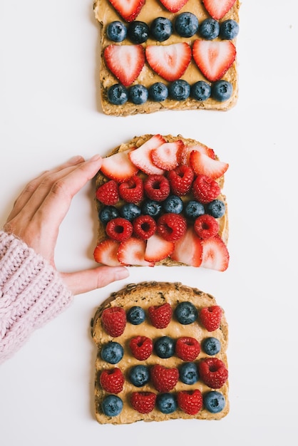 Mano femenina sosteniendo una tostada con pan integral, mantequilla de maní, fresa, arándano, frambuesa