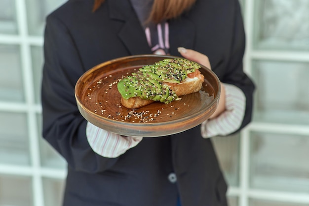 Mano femenina sosteniendo tostadas de aguacate saludable aguacate hass maduro pan integral sésamo semillas de lino vegano