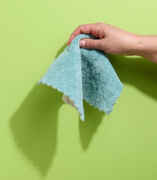 Foto mano femenina sosteniendo un trapo bluew sobre un fondo verde