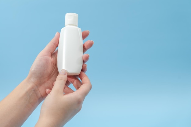 Mano femenina sosteniendo tubos de plástico sobre fondo azul Botellas sosméticas para productos de belleza o medicina