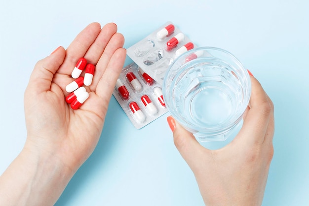 Mano femenina sosteniendo un vaso de agua y pastillas vista superior